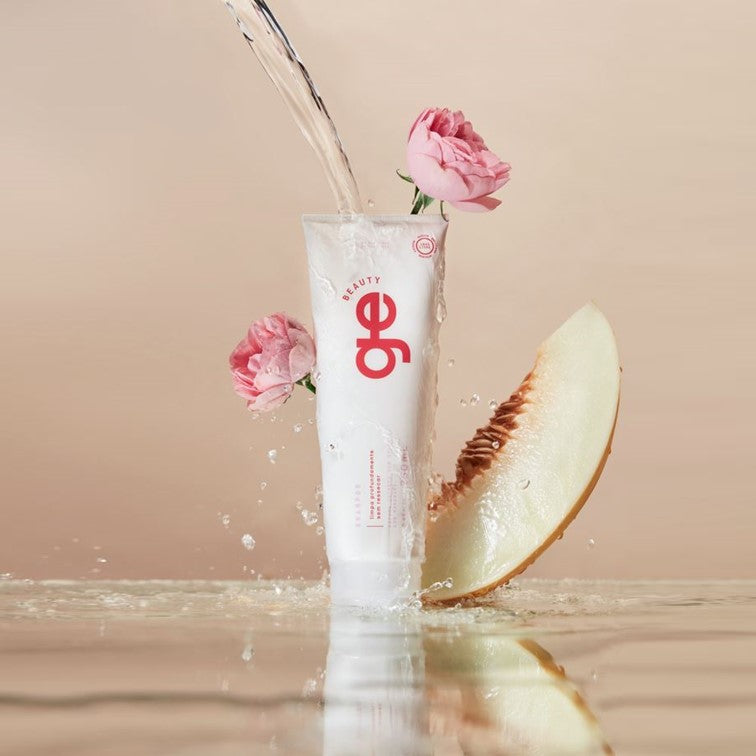 Shampoo sem sulfato GE Beauty em foto produzida com dois de seus principais ingredientes ao fundo: flor de peônia e melão