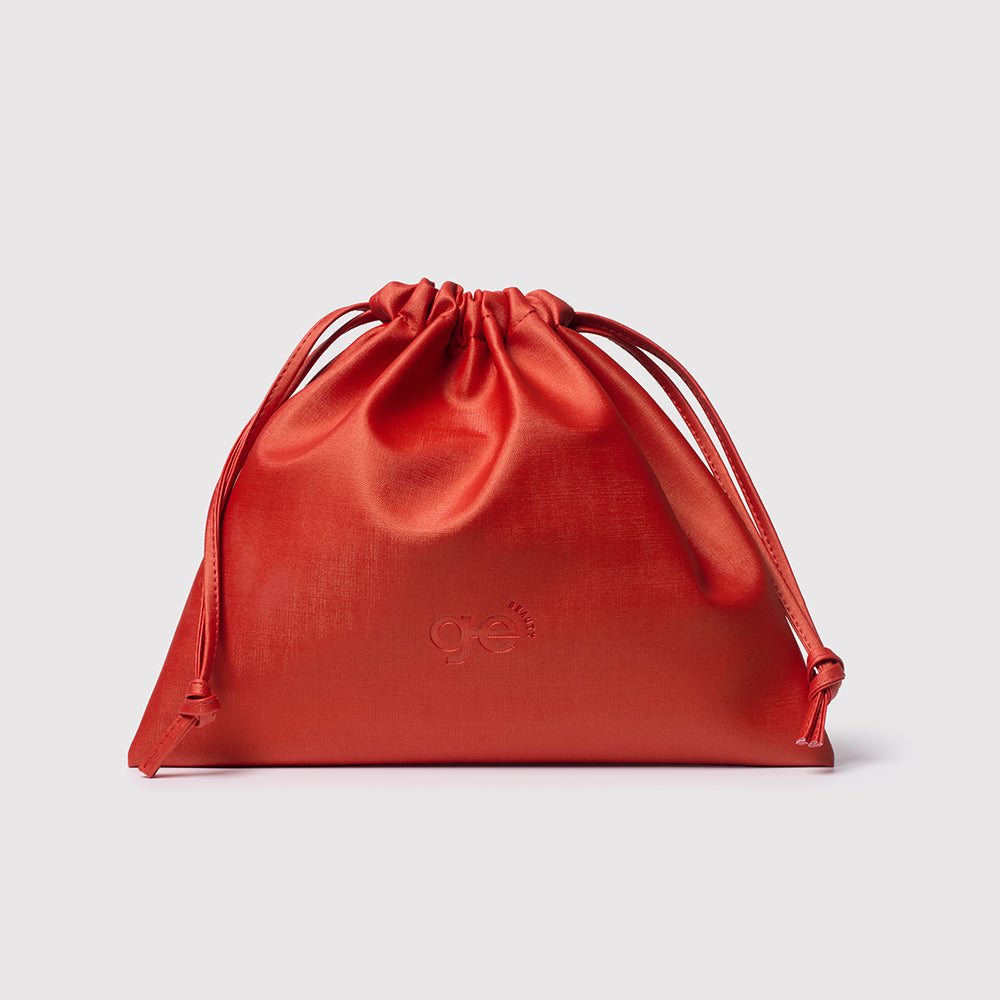 Bolsa de cetim vermelha com logo GE Beauty em fundo cinza claro.